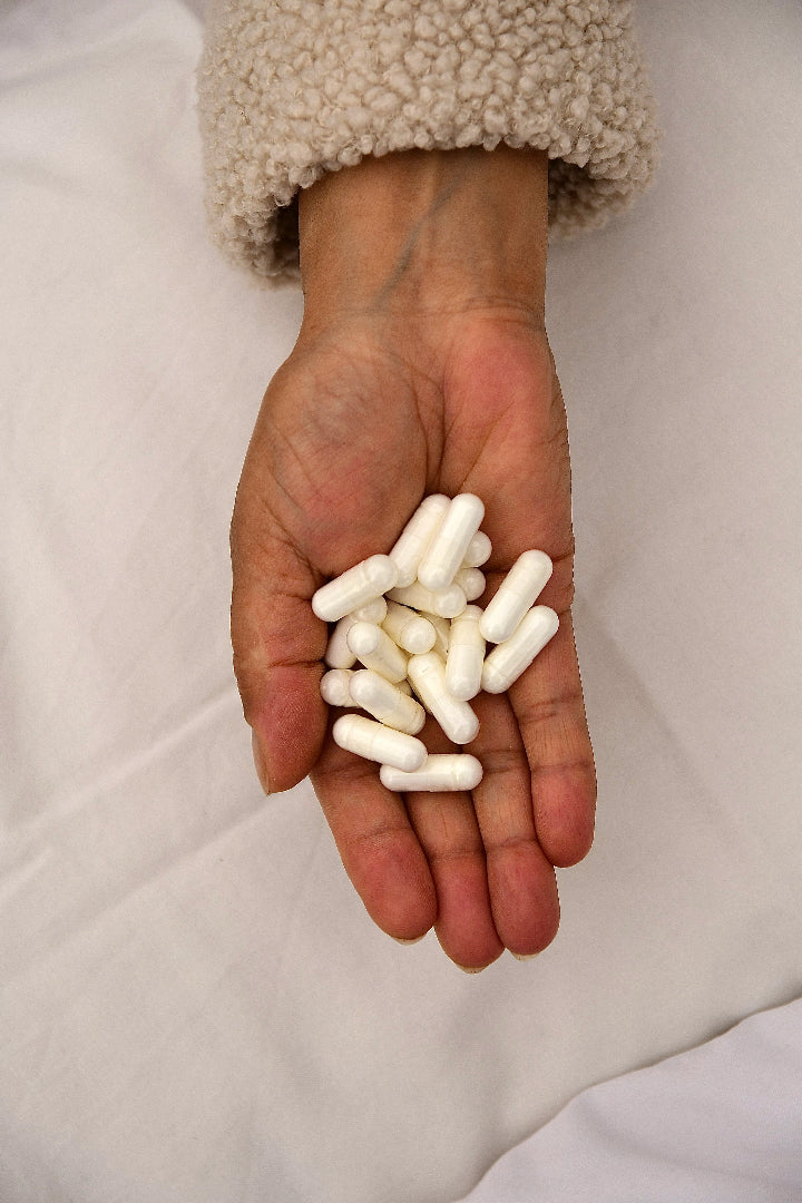 Hand holding white pure sleep supplement capsules against a neutral background